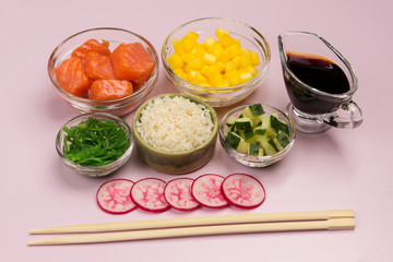 Set of raw vegetables, red fish, rice, soy sauce in glass bowls.