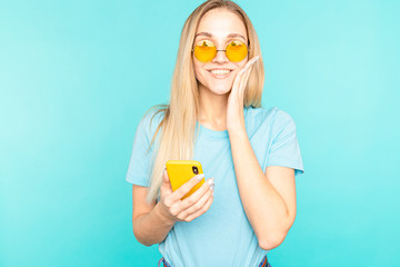 Young woman in glasses standing over blue isolated background looking at the camera. Youth and technology.