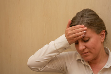 Middle aged woman portrait touching her forehead with hand. 40 years woman not looking at camera. White business shirt is dressed. Sad face and negative emotions