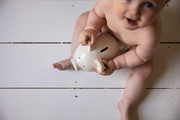 A baby holding onto a piggy ban money box. Childcare costs concept