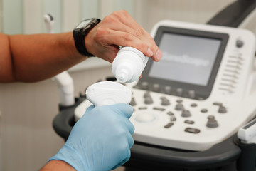 Doctor prepares ultrasound machine add a gel.  Close-up photo. Doctor sonographist hands.