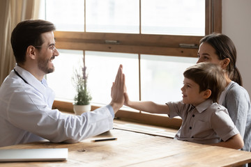 Positive male doctor have fun give high five play with small boy patient visiting with mom, excited...