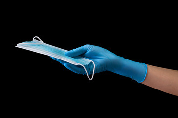 Doctor's hand in medical gloves holding a mask isolated on black