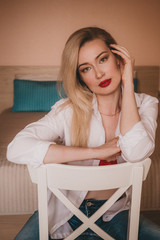 Home portrait of a beautiful young blonde woman in a white shirt, with red lips and expressive eyes. Grain effect. 