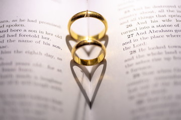 Two wedding Ring on the bible with shadow of heart shape on the page