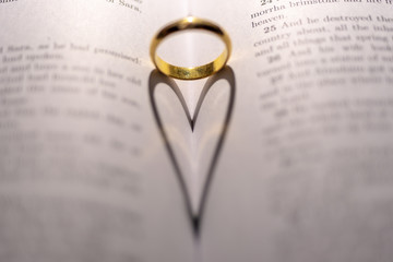 Fototapeta premium A wedding Ring on the bible with shadow of heart shape on the page