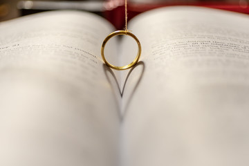 A wedding Ring on the bible with shadow of heart shape on the page