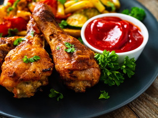 Barbecue chicken drumsticks with vegetables on wooden table
