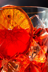 A glass of Campari-based cocktail with ice and an orange slice closeup on a dark background