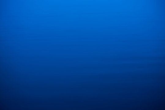 Water ripple nature background. Natural texture of sea of blue classic color. Deep blue calm water in dusk close-up. Meditative image of dense fog above lake. Soft light glitters on water surface.