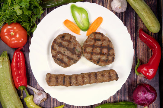 Tasty meatballs and kebabche in a plate on a wooden table, top view
