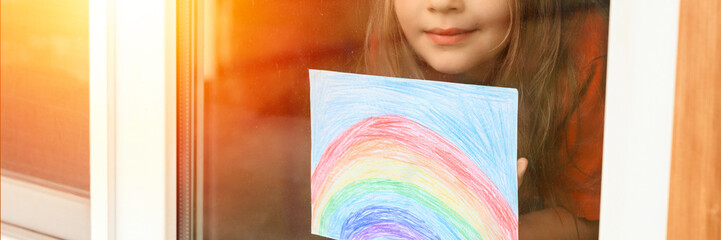 kid girl seven year old with drawing rainbow looks through the window during covid-19 quarantine. stay at home social media campaign for corona virus prevention, let's all be well. flare. banner