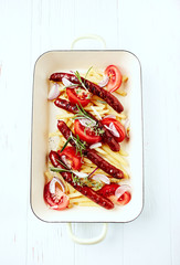 Grilled sausages with french fries, tomatoes and fresh herbs. Bright wooden background. Top view. 