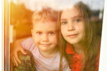 kids siblings boy and girl looks through the window during covid-19 quarantine. stay at home, let's all be well. flare