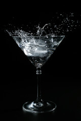 Ice falling on a cocktail glass and splashing. The background is black