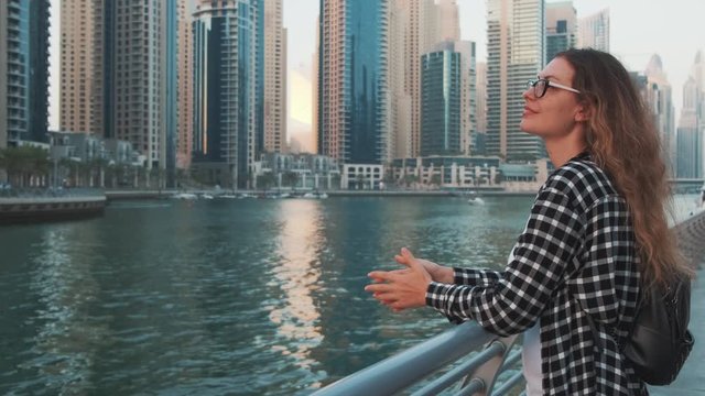 woman tourist standing on promenade Dubai Marina. long red hair. Black white check shirt long sleeves. Girl in glasses admire enjoy beauty white yachts. Backdrop blue bay water, skyscraper buildings