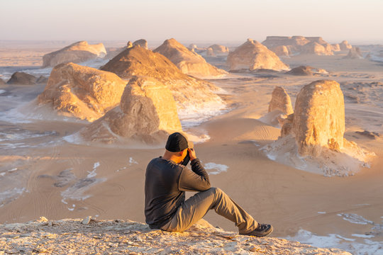 A traveller sitting and taking picture of white desert at sunset, Lower Egypt