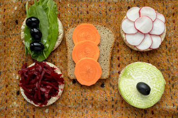 vegetarian sandwiches. on grain loaves lie. repeating the shape of the circle radishes, green radishes, carrots, beets cut into strips, olives, sorrel and orange. it harmonizes with a warm textured da
