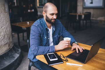 Man with cup of coffee using laptop in sidewalk cafe