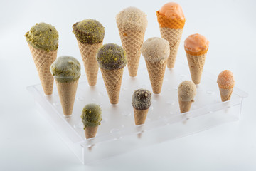 organic handmade ice cream cones in four flavors and different sizes on a stand. The flavors are chocolate, pistachio, caramel and mango. Close up - 349817958