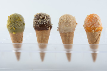 organic handmade ice cream cones in four flavors and different sizes on a stand. The flavors are chocolate, pistachio, caramel and mango. Close up