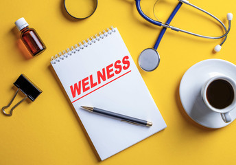 The word wellness is written in a white notebook on a yellow background.