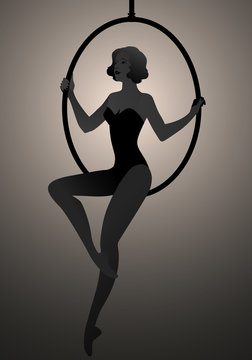 Backlit silhouette of woman trapeze artist sitting on a hoop suspended in the air