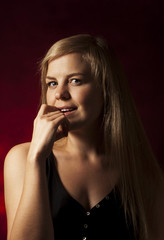 Obraz premium Young beautiful blonde on a dark red background. Close-up of the red lips of a seductive girl raising a finger to her mouth. Flirtation.