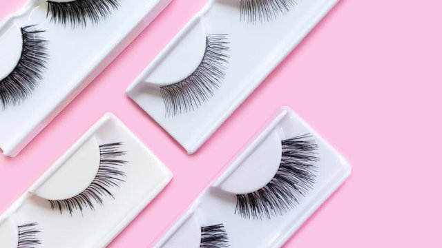 Different false eyelashes on a trendy pastel pink background. Beauty pattern. Makeup accessories. Cosmetics products for women. Bright colorful backdrop. Closeup. Top view, flat lay. Stop motion