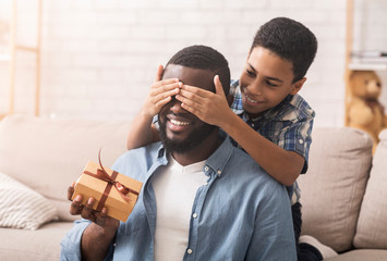 Happy son congratulating his afro dad, covering eyes and giving present