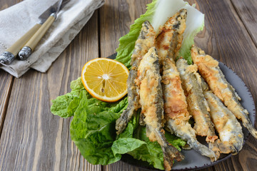 Delicious smelt fried and ready to eat, next to the lemon ring are on a sheet of Beijing cabbage next to cutlery on a napkin