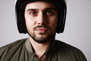 Close-up shot of brutal bearded biker man wears helmet and dressed in a green bomber jacket. Free space for text.