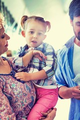 Man looking on boarding pass while his wife is carrying their daughter in airport

