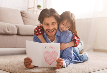 Happy dad reading greeting card while bonding with daughter © Prostock-studio