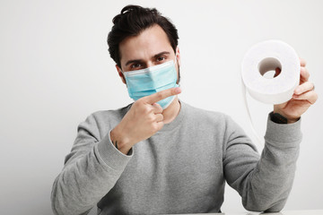 Excited caucasian man in medical mask is happy to have a stock of toilet paper. Stay at home.