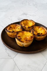 Pasteis de Nata or Belem Tart. Portuguese Custard made with Egg, Cinnamon, Sugar and Flour on Wooden Plate.