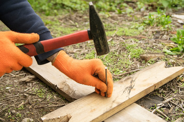 Hands in orange gloves hammer a nail
