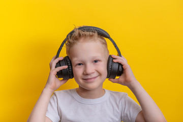 Cute little boy listen music in headphone over yellow background