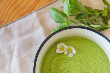 Healthy and vegan greean peas cream soup with some aromatic plants on the backgorund. Summer and fresh food concept. Close up view.