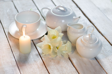 Obraz na płótnie Canvas White daffodils, tea set crockery, burning candle on wooden table