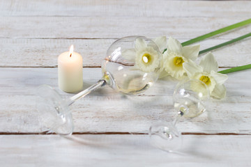 Glasses with white  wine, narcissus flowers, burning candle on wooden background