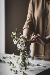 Cherry branches in a vase on the table. The girl in the background makes a bouquet. Spring concept