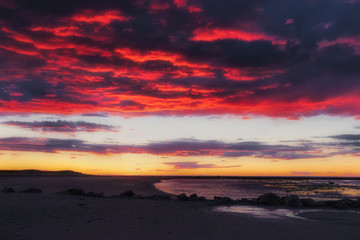 Fototapeta na wymiar Dark red and black cloudy sky at sunset on sand and rocks beach