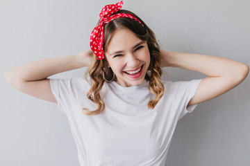 Pleasant caucasian girl in white t-shirt posing in studio. Indoor portrait of laughing gorgeous woman with curly hairstyle.