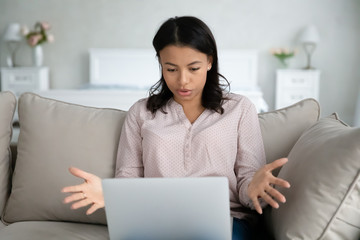 African woman sit on sofa put notebook on lap has problems with device looks at screen feels...