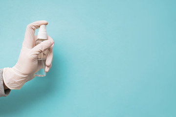 Woman's hand in medical protective glove hand holding sanitizer spay bottle on blue background