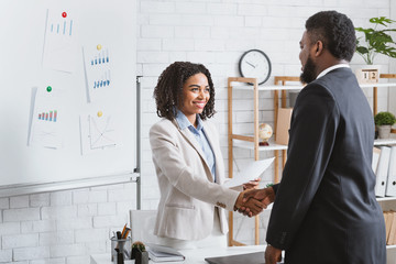 Smiling HR manager shaking hands with young applicant at job interview in office. Blank space