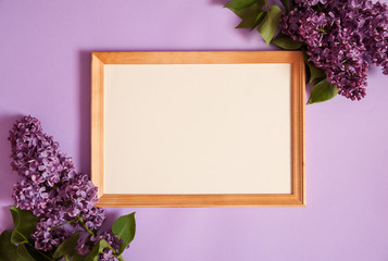 Flower composition. Wooden photo frame and border of spring lilac flowers (Syringa vulgaris) on a light purple background. Top view.