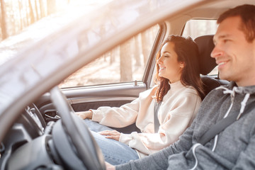 Happy young family rides in a car in the forest. A man is driving a car, and his wife is sitting...
