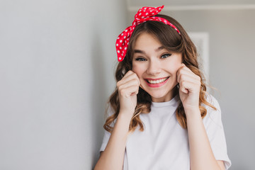 Cute girl with trendy hairstyle fooling around in studio. Indoor shot of beautiful inspired lady making funny faces.